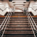 Symmetrical underground staircase leading to a New York subway entrance, featuring metal railings and white tile walls.