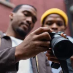 Close-up of two men examining a DSLR camera outdoors in a city environment.